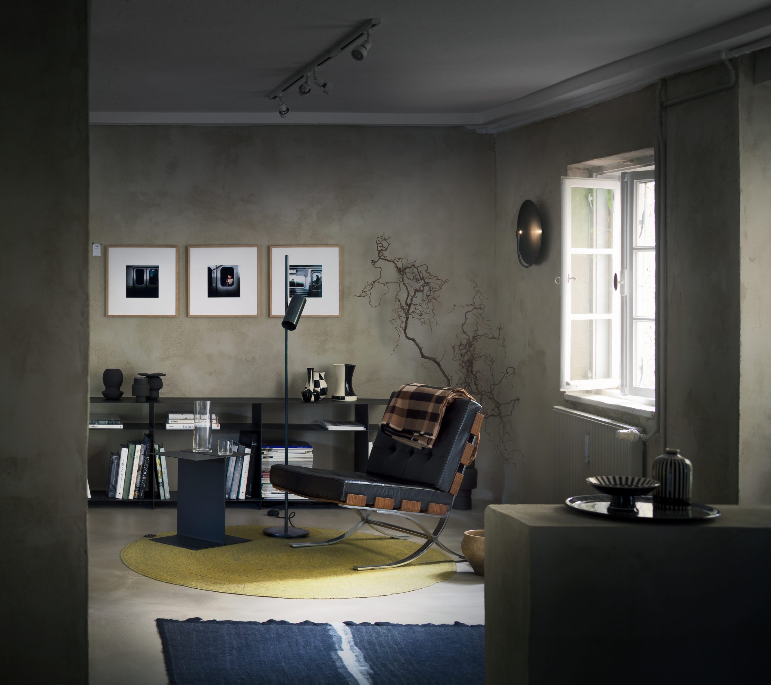 Gemütliche Interior-Szene im PEAM Showroom mit ikonischem Designstuhl, runder Teppichinsel, skulpturalen Vasen, Bücherregal und Kunstfotografien – stilvolles Zusammenspiel aus Designklassikern und kuratierter Wohnästhetik