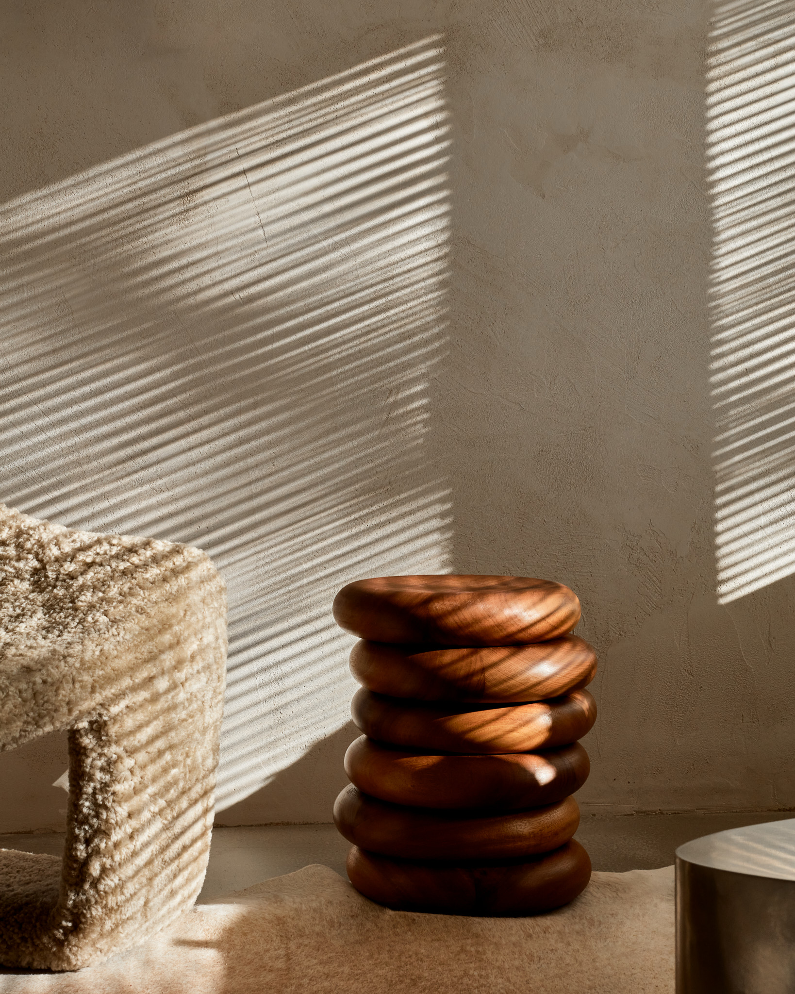 Tiny Apartment Schattenspiel Jalousie Vintage Fellsessel Sichtestrich Massivholzhocker Slice gespachtelte Wände mit Kalkputz monochromes Interior Wabi Sabi