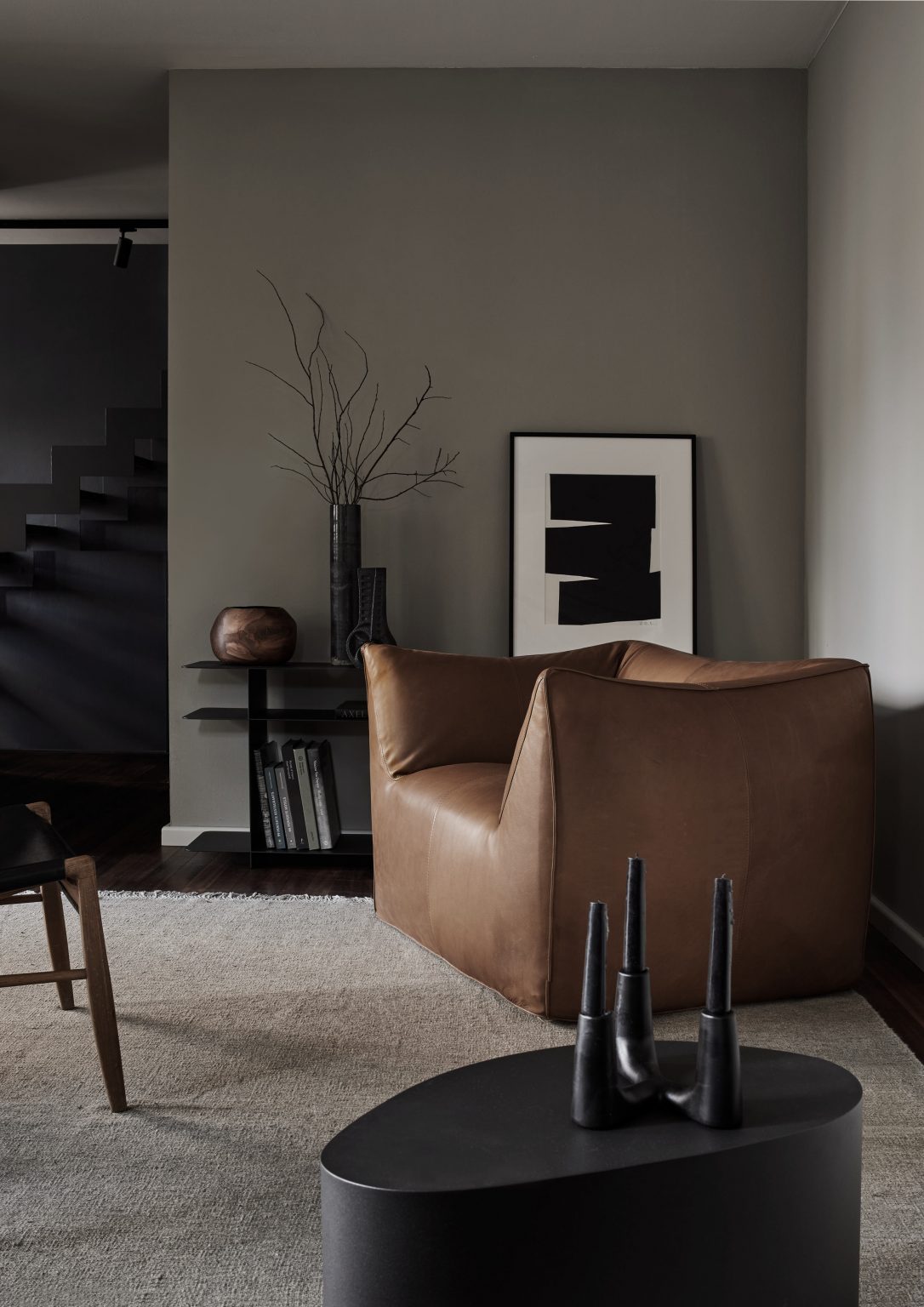 Elegantes Wohnzimmer mit skulpturalem Ledersessel in Cognac, dunklem Beistelltisch, minimalistischer Wandkunst und monochromer Raumgestaltung im modernen Interior Design