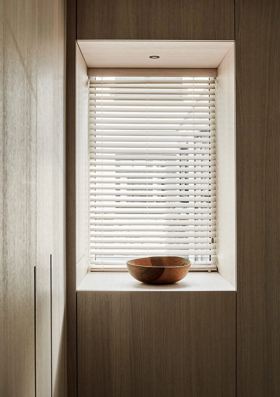 Handgedrechselte Holzschale aus Nussbaum auf einer Fensterbank mit Holzverkleidung und weißen Jalousien – minimalistisches Wohnaccessoire in ruhiger, natürlicher Umgebung