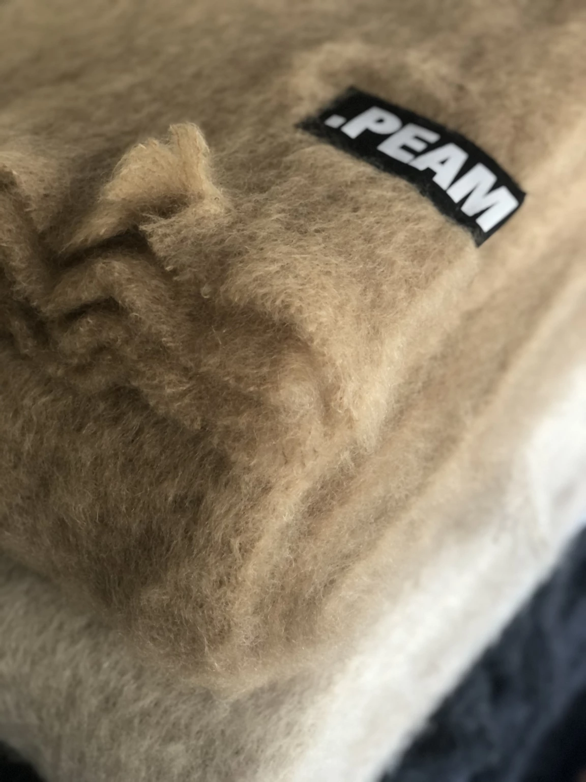 Detailaufnahme gefalteter Wolldecken in Naturtönen mit PEAM-Label – hochwertige Wohntextilien aus weicher Alpakawolle, gestapelt im minimalistischen Interior-Kontext