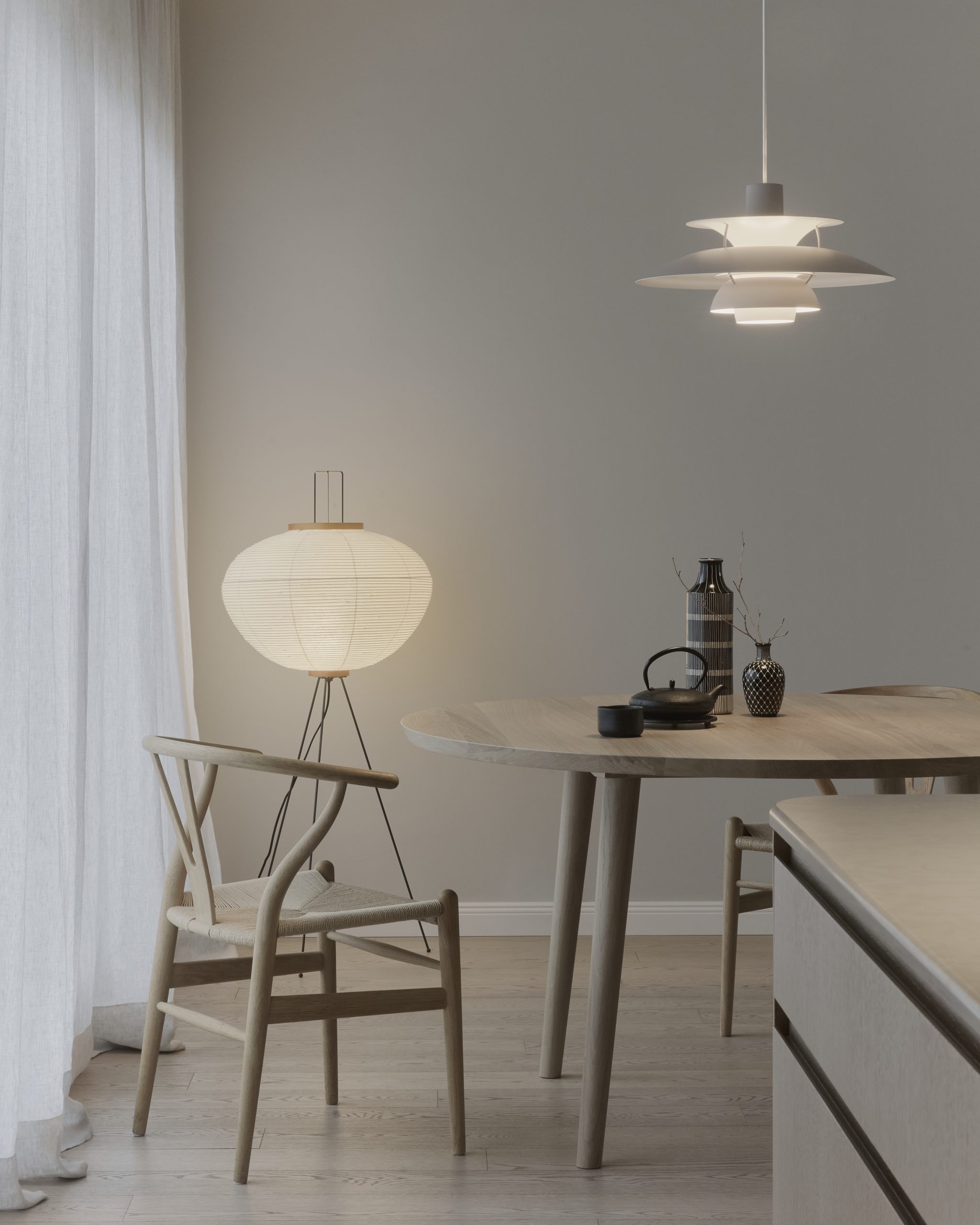 Lichtdurchfluteter Essbereich im skandinavischen Stil mit hellem Massivholztisch, Wishbone Chair, japanisch inspirierter Stehleuchte und minimalistischer Pendelleuchte in sanfter Atmosphäre.